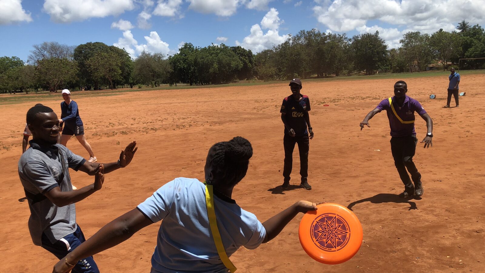 Kuvassa näkyy henkilöitä heittelemässä frisbeetä urheilukentällä Tansaniassa.
